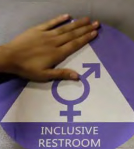 hand on top of a sign for an inclusive restroom