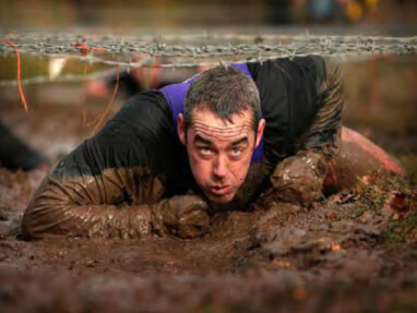 man crawling through the mud under barbed wire
