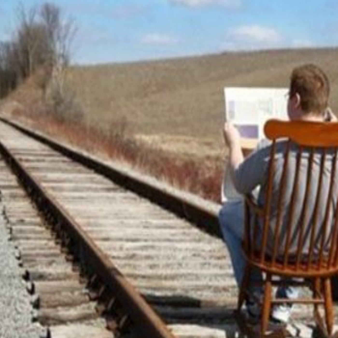 man sitting in chair on train tracks reading newspaper